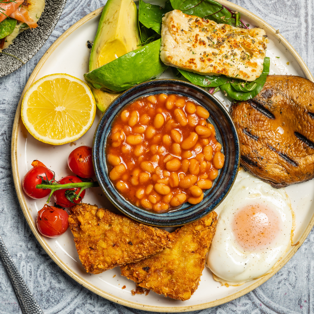 A breakfast plate with grilled halloumi, avocado, beans, hash browns, a fried egg and tomatoes